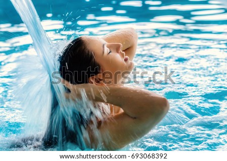 Close up portrait of young girl with relaxed facial expression under high pressure shower in spa.Woman touching hair with eyes closed.