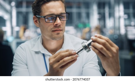 Close Up Portrait Of Young Handsome Engineer In Glasses Working On Manufacturing Metal Parts In Office At Car Assembly Plant. Industrial Product Designer Examining Prototype Parts Before Production.