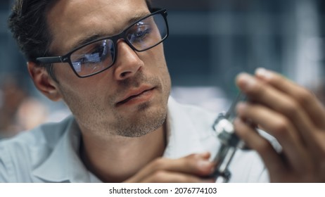 Close Up Portrait Of Young Handsome Engineer In Glasses Working On Manufacturing Metal Parts In Office At Car Assembly Plant. Industrial Product Designer Examining Prototype Parts Before Production.