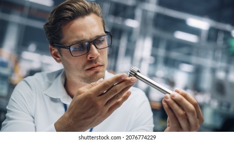 Close Up Portrait Of Young Handsome Engineer In Glasses Working On Manufacturing Metal Parts In Office At Car Assembly Plant. Industrial Product Designer Examining Prototype Parts Before Production.