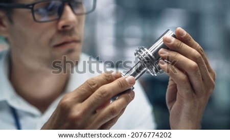 Close Up Portrait of Young Handsome Engineer in Glasses Working on Manufacturing Metal Parts in Office at Car Assembly Plant. Industrial Product Designer Examining Prototype Parts Before Production.