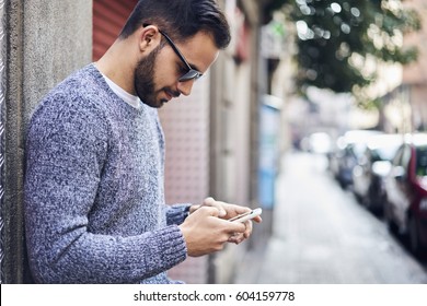 Close up portrait of young handsome male hipster in trendy wear resting during weekends booking tickets in movie waiting for girlfriend for dating using smartphone and fast 5G wireless connection