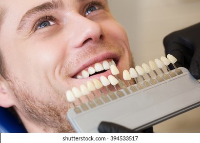 Close up portrait of Young man in dentist chair, Check and select the color of the teeth. Dentist makes the process of treatment in dental clinic office.Dentist