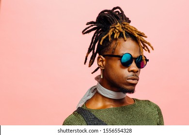 Close up portrait of a young man in green with dreadlocks and blue sunglasses, isolated on pink - Shutterstock ID 1556554328