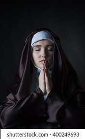 Close up portrait of young nun. Nun is praying. Photo on black background.
