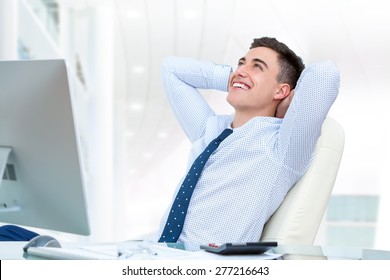 Close up portrait of young office worker relaxing in office. Young man sitting at desk with hands behind head and looking up.