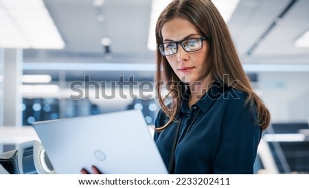 Close Up Portrait of a Young Robotics Engineer Using Laptop Computer, Analyzing Robotic Machine Concept in a High Tech Factory. Female Scientist Manipulate and Program the Robot for Work.