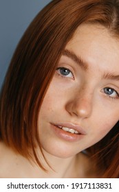 Close up portrait of young serious woman without make up with short ginger hair and naked shoulders is looking at the camera while posing with grey background. Stock photo