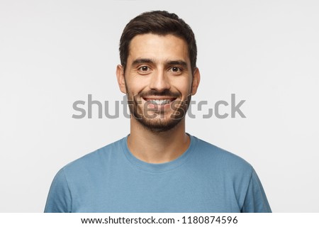 Close up portrait of young smiling handsome guy in blue t-shirt isolated on gray background