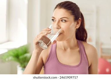 Close up portrait of a young sporty happy woman standing at home after working out drinking a water, looking cheerful and smiling. Sport, fit, healthy nutrition and lifestyle concept. - Powered by Shutterstock