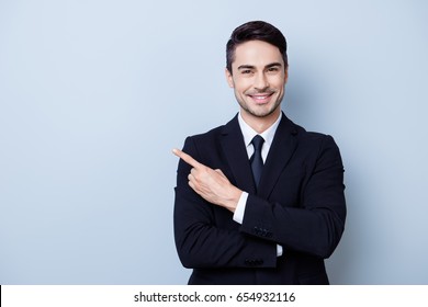 Close up portrait of young successful brunete  stock-market broker guy on the pure light blue background, he is smiling, wearing suit with tie and is pointing on a copyspace with his finger - Powered by Shutterstock