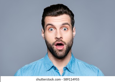 A close up portrait of a young surprised man with opened mouth isolated on gray background.