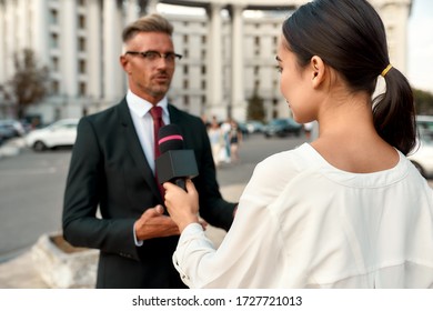 Close Up Portrait Of Young Woman Conducting Journalistic Interview Of Cheerful Politician. People Making Interview Using Equipment Set At Outdoor Location. Horizontal Shot. Selective Focus On Woman