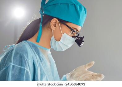 Close up portrait of a young woman doctor dentist with dental binocular loupes on her face wearing blue mask and medical uniform at work in dentistry clinic. Dental health care concept. - Powered by Shutterstock