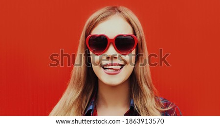Close up portrait of young woman teasing wearing a red heart shaped sunglasses over background