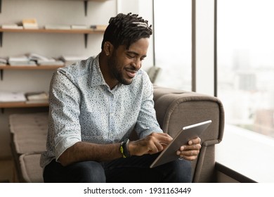 Close up positive African American young man using tablet, having fun, sitting on couch at home, browsing apps, chatting, spending leisure time with gadget, satisfied customer shopping online - Powered by Shutterstock