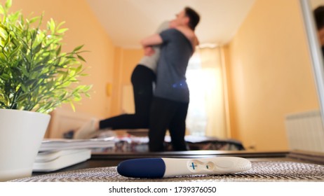 Close up of positive pregnancy test lying on a table and woman embracing a man. Stock footage. Happy husband hugging his pregnant wife in the room, family concept.