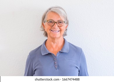 close up and potrait of mature woman smiling and looking at the camera with a white wall at the background - active senior concept and lifestyle