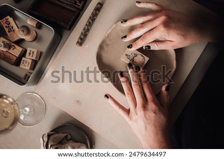 Close up of pottery course attendee's hands decorating clay plate with stamp. From above view of creative craftswoman decorating and imprinting artistic stamp at pottery workshop.Hands doing clay work