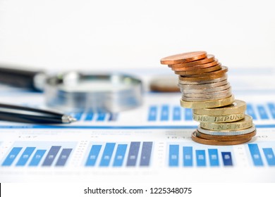 Close up pound sterling coins stacking on capital graph with pen and magnifier glass for investment concept.
