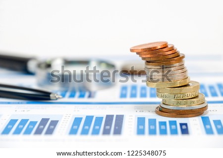 Close up pound sterling coins stacking on capital graph with pen and magnifier glass for investment concept.