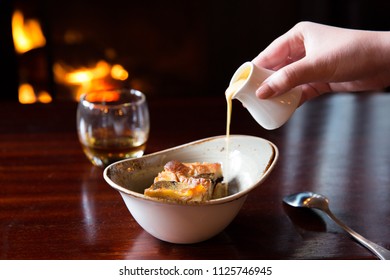 Close Up Of Pouring Custard Over Bread And Butter Pudding Dessert