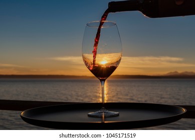 Close up pouring red wine at sunset on seaside view deck landscape.