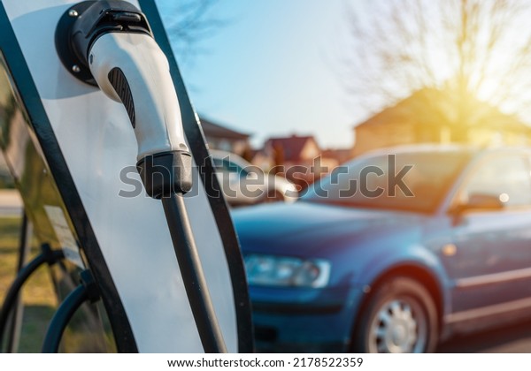 Close up power cord\
for electric car. Green station.Power supply for electric car\
battery charging.Blurred car,sunset in the background.Selective\
focus.Closeup.
