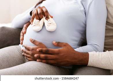 Close up of pregnant black woman belly with baby shoes on it, husband hugging his wife, new family concept