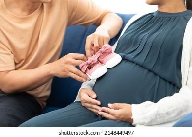 close up of pregnant woman belly and her husband  showing small shoes for newborn baby