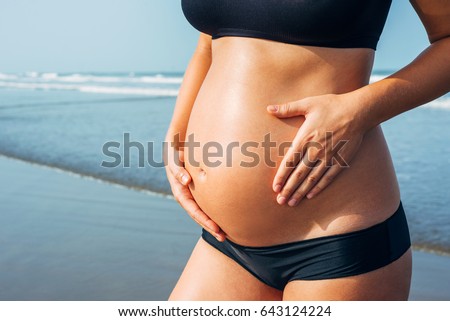 Close up of pregnant woman belly wearing black bikini on the sea background