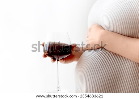Close Up Of Pregnant Woman  Drinking. Pregnant woman with glass of red wine in hand indoors.
