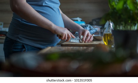 Close up pregnant woman with knife on kitchen cuts mushrooms