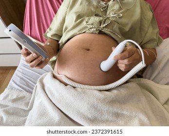 close up pregnant woman patient using fetal droppler device to listening baby heartbeat on a bed in hospital