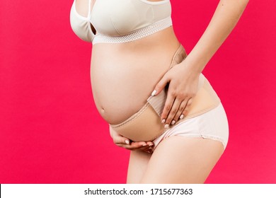 Close up of pregnant woman in underwear with bandage against backache at pink background with copy space. Mother is suffering from pain in the back. Orthopedic abdominal support belt concept. - Shutterstock ID 1715677363