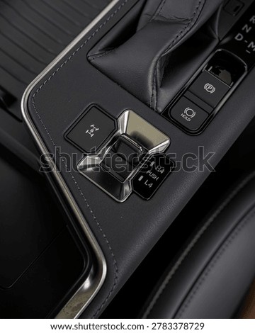 Close up of a premium car interior featuring a polished gear shifter, chrome accents, leather trim and surrounding electronic controls.