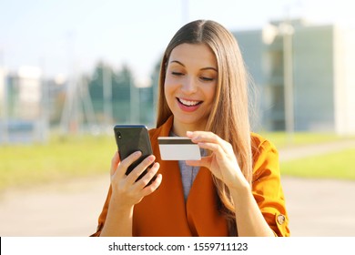 Close up of pretty woman reading credit card number doing online payment with her mobile phone outside.