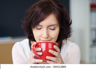Close up Pretty Young Office Woman Smelling the Aroma of her Coffee Drink in a Red Cup with Eyes Closed.