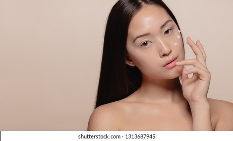 Close up of a pretty young woman applying cream to her face. Korean female model putting moisturizer cream on her face skin.