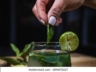 Close Up Of Professional Anonymous Barman Squeezing Lime With Hand While Making Mojito Cocktail. Worker Woman Preparing Cocktails At Home