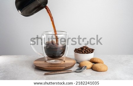 Close up professional barista pouring freshly brewed drip coffee in a glass mug. Preparing coffee alternative method. With biscuits and fresh coffee beans.