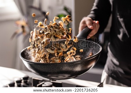 Close up of professional Chef cook hands roasts champignons with cream in wok pan for Mediterranean cuisine. Flying mushrooms in motion levitation. 