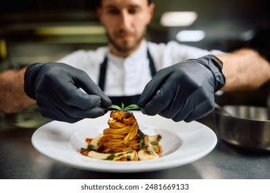 Close up of professional chef serving pasta while working in the kitchen. 