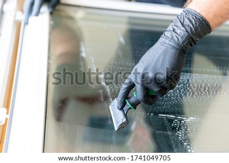 A close up of a professional cleaneer using a diamond blade scraper to clean a window