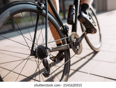 Close Up Of Professional Cyclist With Muscular Legs Using Black Sport Bike For Training Outdoors. Focus On Wheels. Regular Workout Of Sportsman.