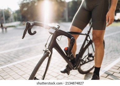 Close Up Of Professional Cyclist In Sport Clothes Resting On His Bike After Training Outdoors. Summer Sunlight On Background. Active Lifestyles Concept.