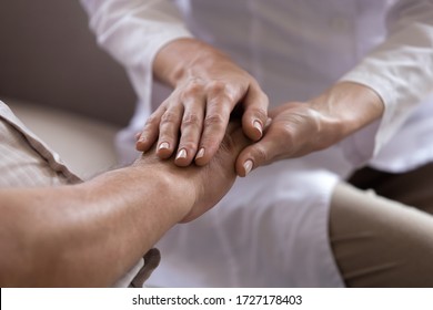 Close up of professional female caregiver hold senior male patient hands showing support and empathy at nursing home, caring doctor or nurse comfort support mature man, elderly healthcare concept