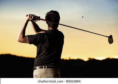 Close up professional golf player in black shirt teeing-off ball in twilight, view from behind. - Powered by Shutterstock