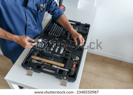 Close up of professional handyman in uniform with open tool bag sitting on home kitchen floor 