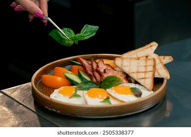 close up in a professional kitchen on a clean metal table woman chef collects English breakfast on a round wooden plate decorated - Powered by Shutterstock